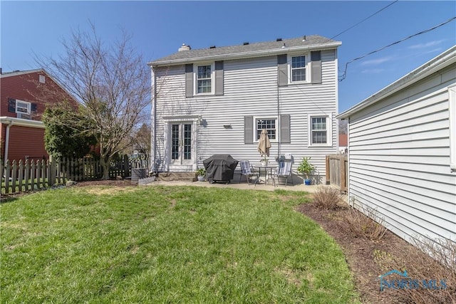 rear view of house featuring fence, a patio, a lawn, and a chimney