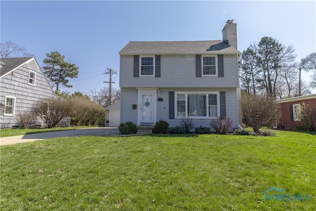 colonial-style house featuring a front yard, a chimney, and a detached garage