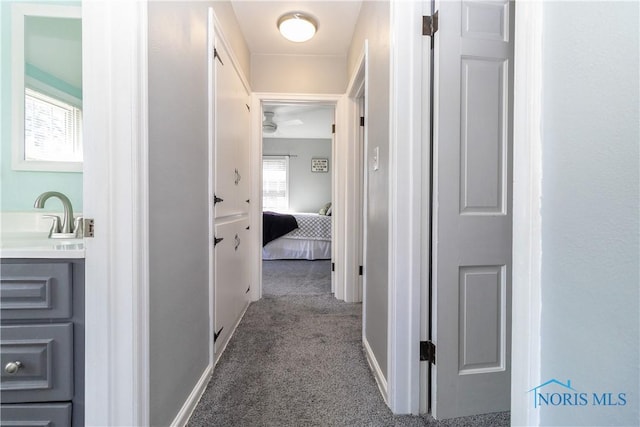 corridor featuring carpet flooring, a sink, and baseboards