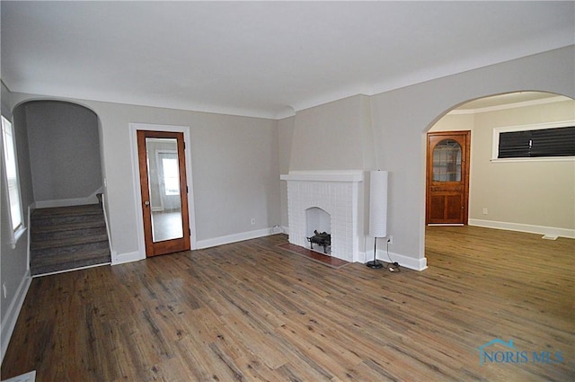 unfurnished living room featuring stairway, a brick fireplace, baseboards, and wood finished floors