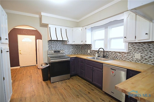 kitchen featuring arched walkways, a sink, ornamental molding, wooden counters, and appliances with stainless steel finishes
