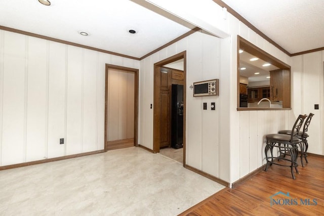 empty room with ornamental molding, wood finished floors, a decorative wall, and baseboards