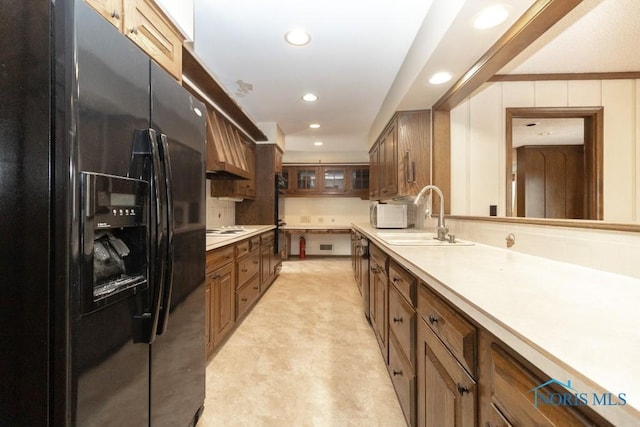 kitchen with glass insert cabinets, a sink, light countertops, black appliances, and recessed lighting