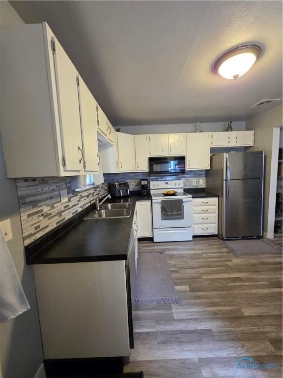 kitchen featuring a sink, white range with electric cooktop, freestanding refrigerator, dark countertops, and black microwave