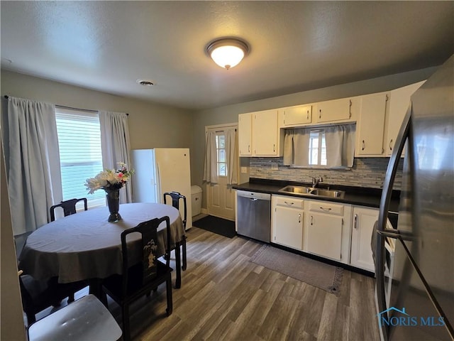 kitchen with backsplash, dark countertops, a sink, stainless steel appliances, and dark wood-style floors