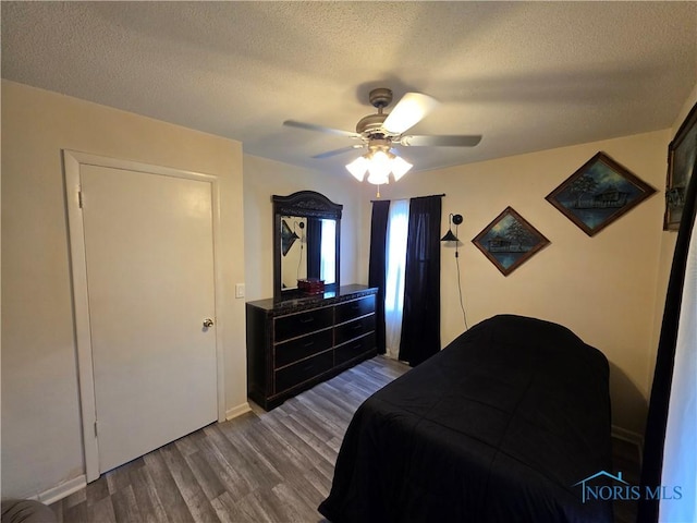bedroom featuring baseboards, dark wood-style floors, a textured ceiling, and a ceiling fan