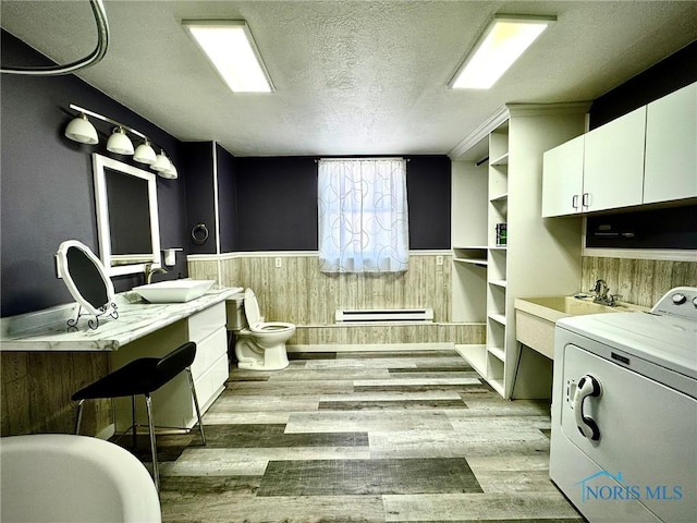 106 Adrian St, Delta, OH 43515 - bathroom featuring washer / clothes dryer, wainscoting, a textured ceiling, baseboard heating, and wood finished floors
