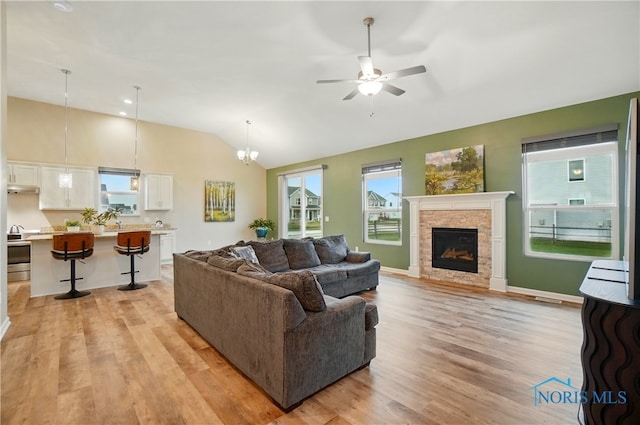 living room featuring a fireplace, a ceiling fan, vaulted ceiling, light wood finished floors, and baseboards