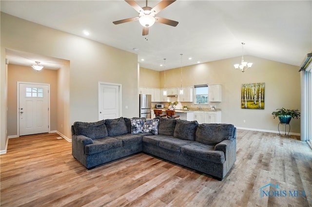 living area featuring light wood-style flooring, ceiling fan with notable chandelier, and baseboards