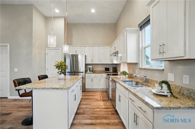 kitchen featuring white cabinetry, a kitchen island, a sink, stainless steel appliances, and a breakfast bar area