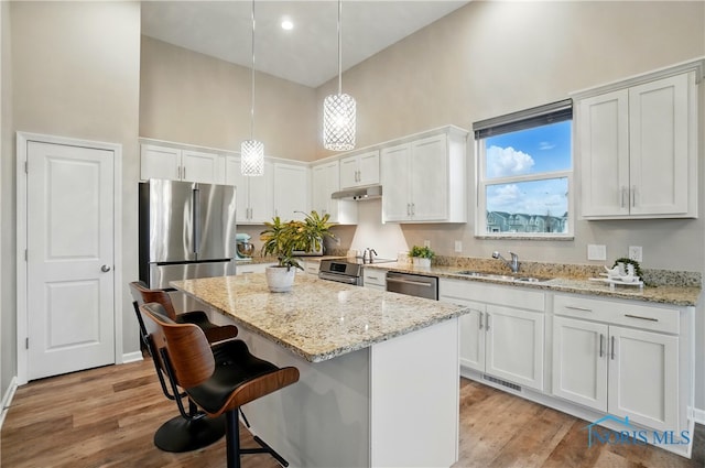 kitchen featuring a towering ceiling, a kitchen island, under cabinet range hood, a sink, and stainless steel appliances