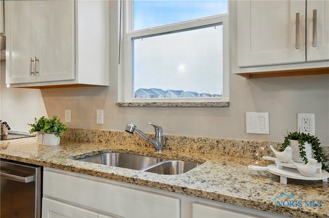kitchen featuring stainless steel dishwasher, a sink, white cabinetry, and light stone countertops