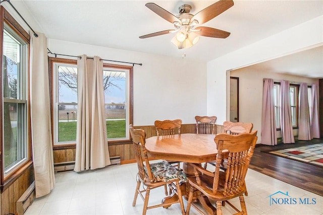 dining area with ceiling fan, a baseboard radiator, wooden walls, a wainscoted wall, and a baseboard heating unit