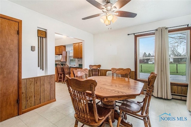 dining area with a ceiling fan, light tile patterned floors, wooden walls, and wainscoting