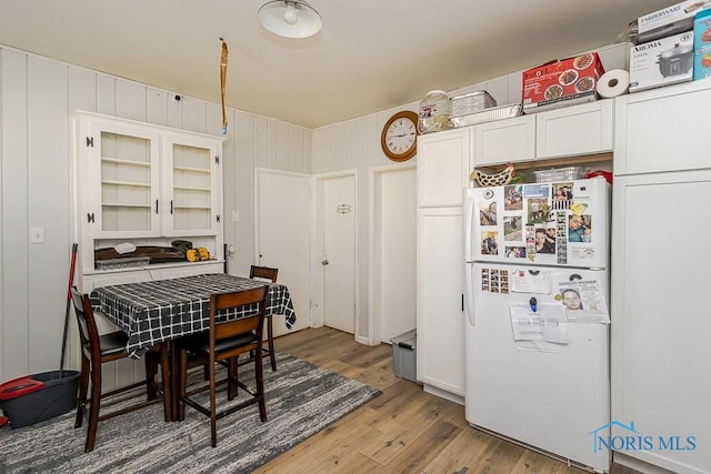 kitchen featuring glass insert cabinets, white cabinets, freestanding refrigerator, and wood finished floors
