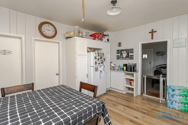 bedroom with a decorative wall, freestanding refrigerator, and light wood-style floors