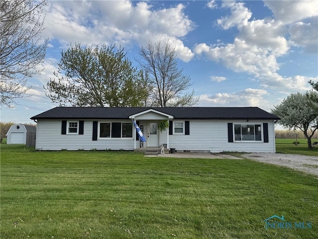 ranch-style home with entry steps, gravel driveway, a front lawn, and an outbuilding