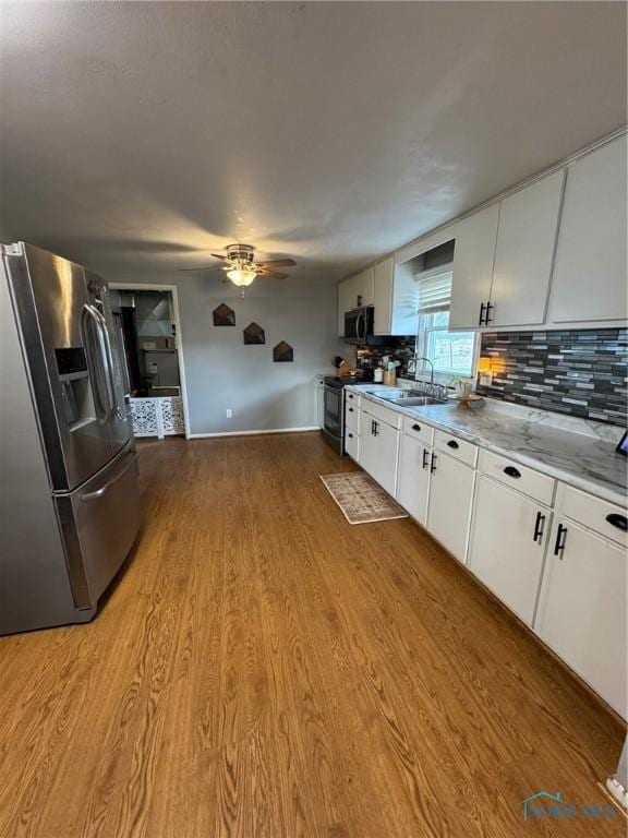 kitchen featuring stainless steel appliances, light wood-style floors, a sink, white cabinetry, and a ceiling fan