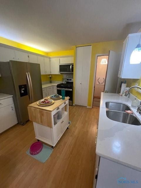 kitchen featuring a sink, light countertops, light wood-style floors, white cabinetry, and stainless steel appliances