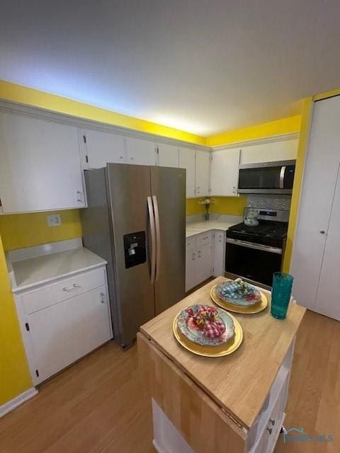 kitchen with light wood-type flooring, white cabinets, a center island, light countertops, and stainless steel appliances