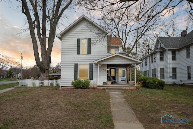 traditional-style house featuring a porch, a front yard, and fence