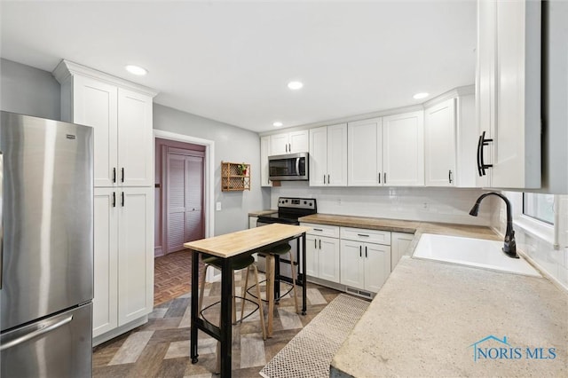 kitchen with white cabinets, a sink, light countertops, recessed lighting, and stainless steel appliances