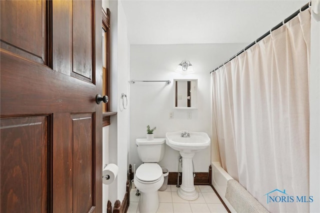 bathroom featuring baseboards, shower / bath combo, tile patterned flooring, toilet, and a sink
