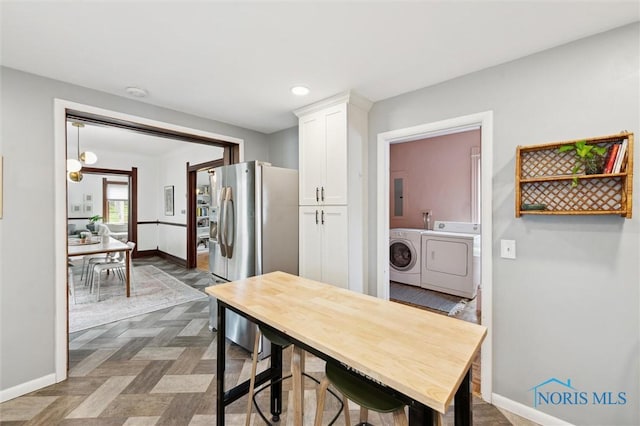 kitchen featuring baseboards, stainless steel fridge, washer and dryer, electric panel, and white cabinetry