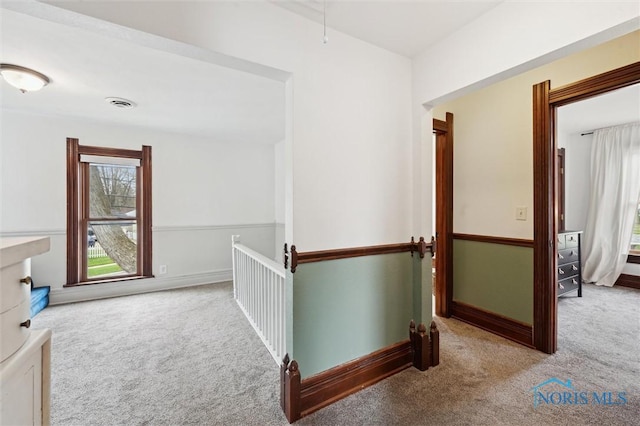 hallway with carpet flooring, visible vents, an upstairs landing, and baseboards