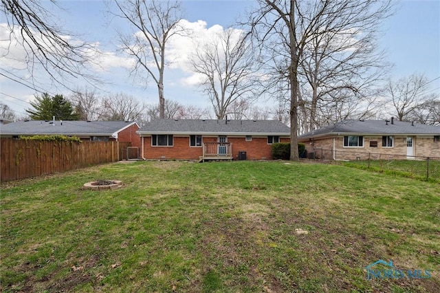 back of house with a wooden deck, a yard, a fenced backyard, a fire pit, and brick siding