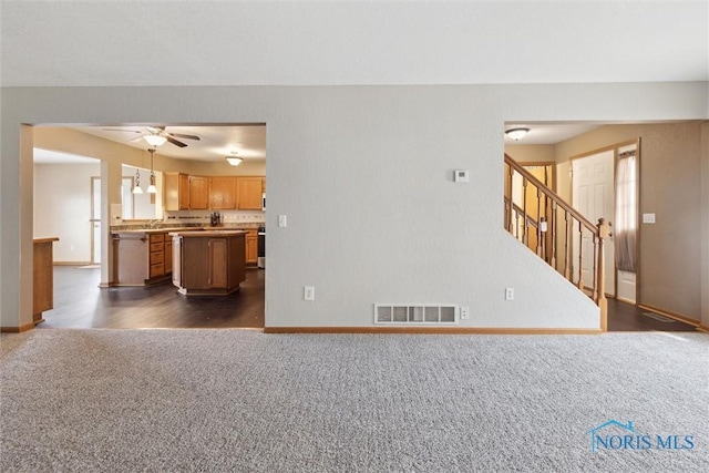 unfurnished living room with baseboards, ceiling fan, dark colored carpet, and visible vents