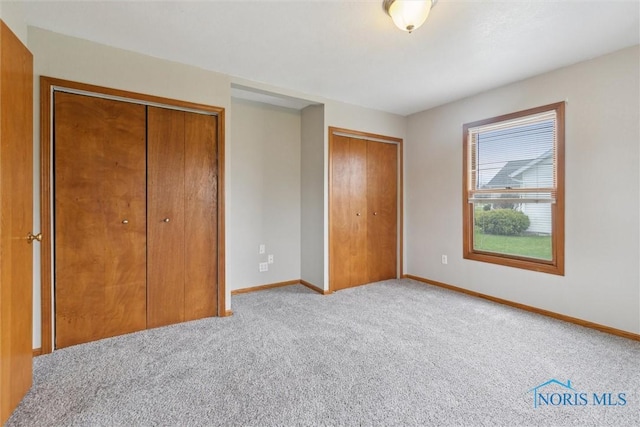 unfurnished bedroom with baseboards, carpet flooring, and two closets