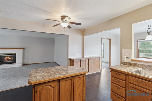 kitchen featuring light countertops, a brick fireplace, brown cabinets, ceiling fan, and a sink