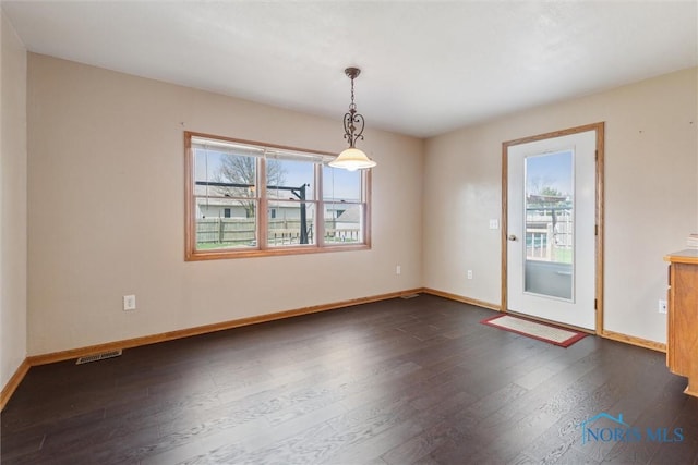 spare room with dark wood-style flooring, visible vents, and baseboards