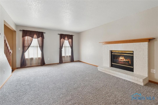 unfurnished living room with carpet flooring, a brick fireplace, a textured ceiling, and baseboards