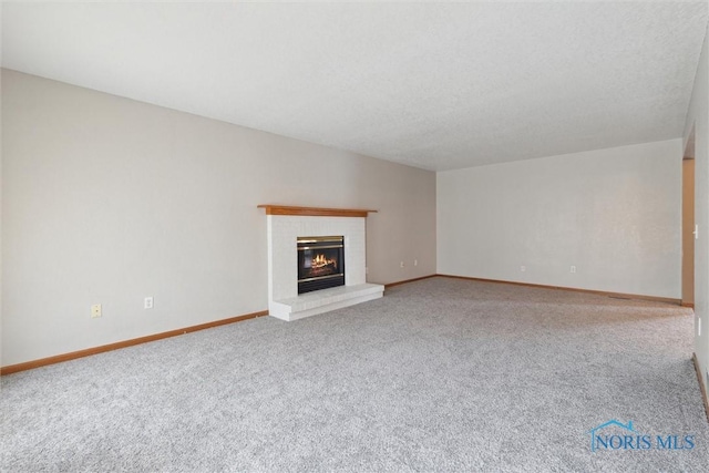 unfurnished living room with a brick fireplace, baseboards, a textured ceiling, and carpet floors