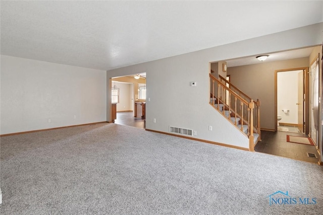 unfurnished living room with stairway, visible vents, and carpet floors