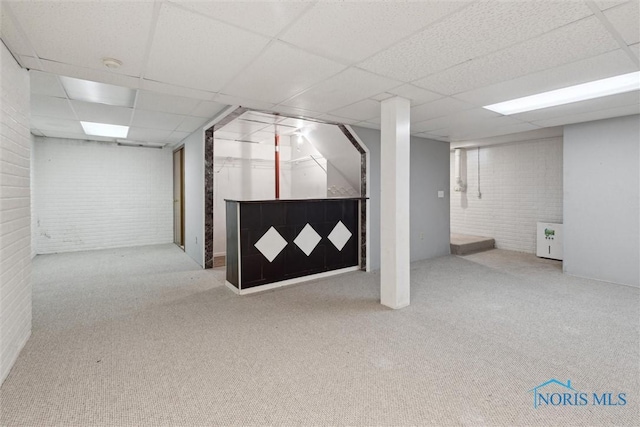 finished basement with a paneled ceiling, carpet, and brick wall