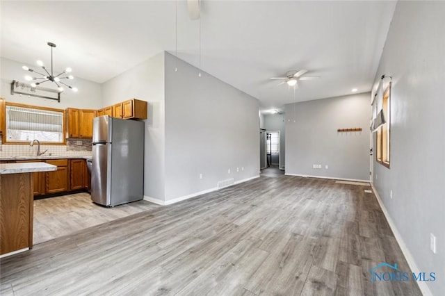unfurnished living room with visible vents, baseboards, light wood finished floors, and ceiling fan with notable chandelier