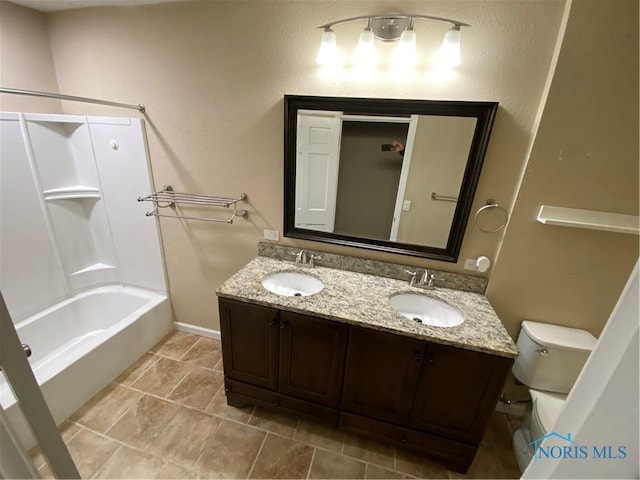 bathroom with toilet, baseboards, double vanity, and a sink