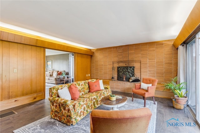 living room with visible vents, wood walls, a brick fireplace, and wood finished floors