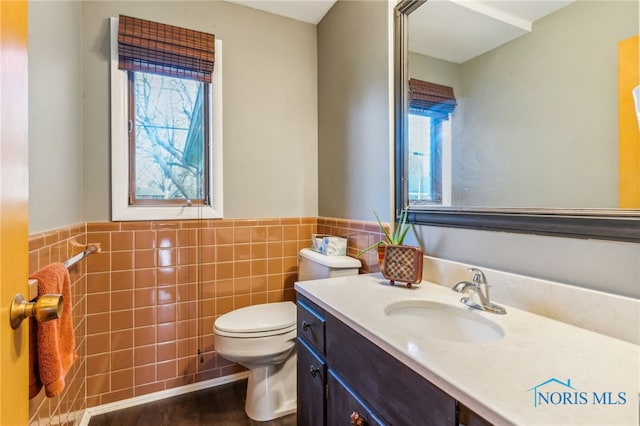 half bath with vanity, toilet, tile walls, and a wainscoted wall