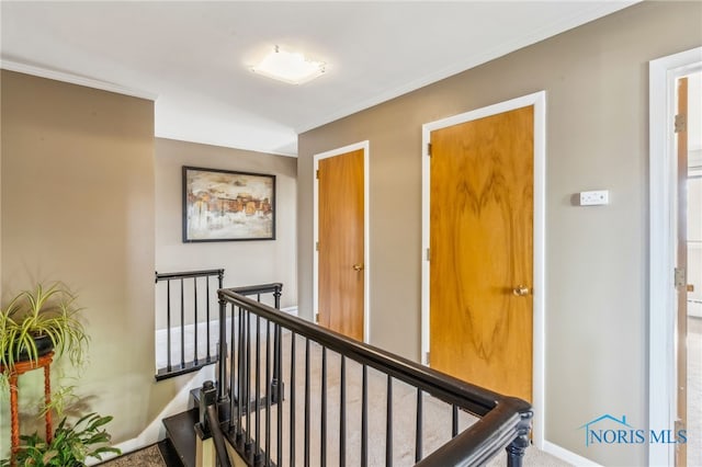 corridor with baseboards, ornamental molding, carpet, and an upstairs landing