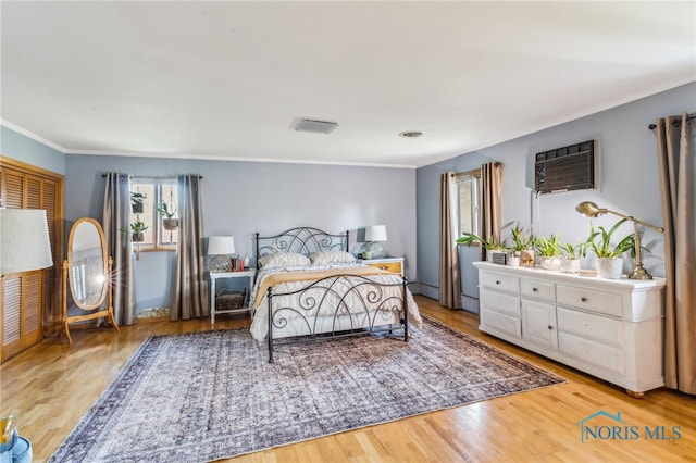 bedroom with a wall mounted AC, ornamental molding, wood finished floors, and visible vents