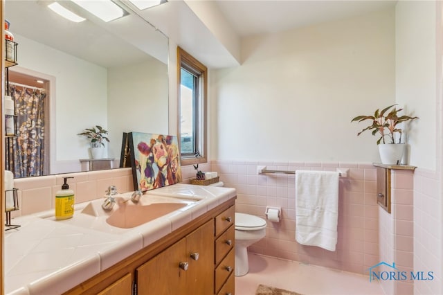 bathroom with toilet, tile walls, wainscoting, and vanity