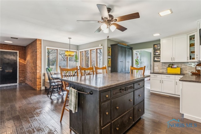 kitchen with a breakfast bar, ceiling fan, white cabinetry, tasteful backsplash, and dark wood finished floors