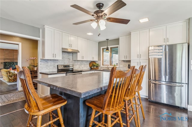 kitchen featuring dark countertops, tasteful backsplash, stainless steel appliances, a ceiling fan, and a kitchen bar