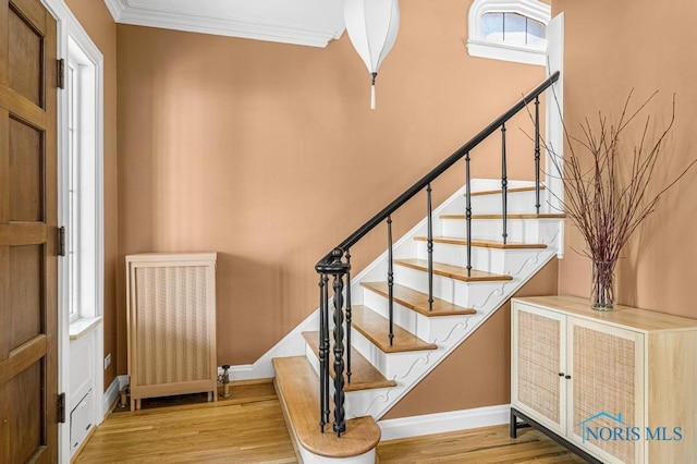 staircase featuring radiator heating unit, baseboards, crown molding, and wood finished floors