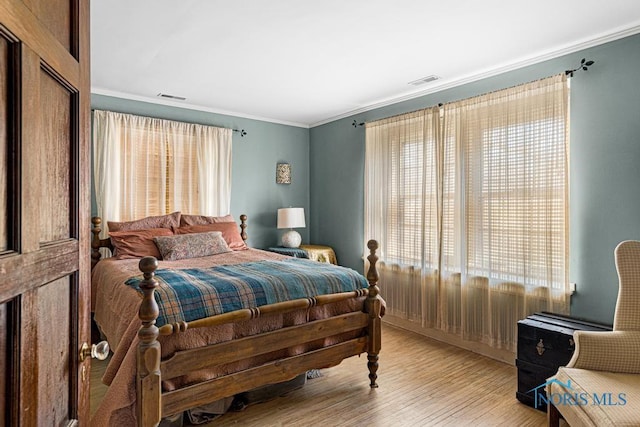 bedroom with crown molding, visible vents, and wood finished floors