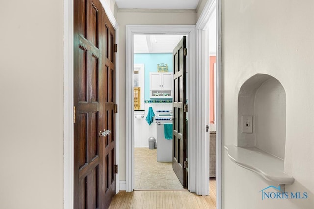 hallway with ornamental molding and light wood-style flooring